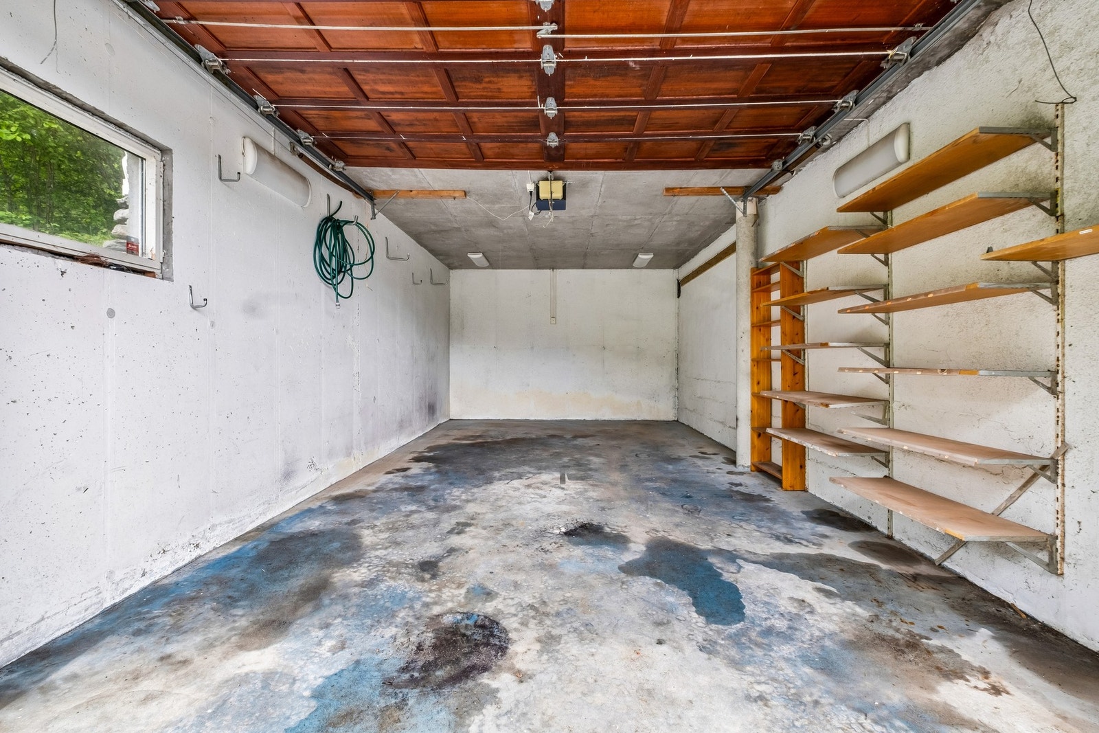 Garasje med betonggulv, vippeport og hyller monter på vegg. Galleribilde