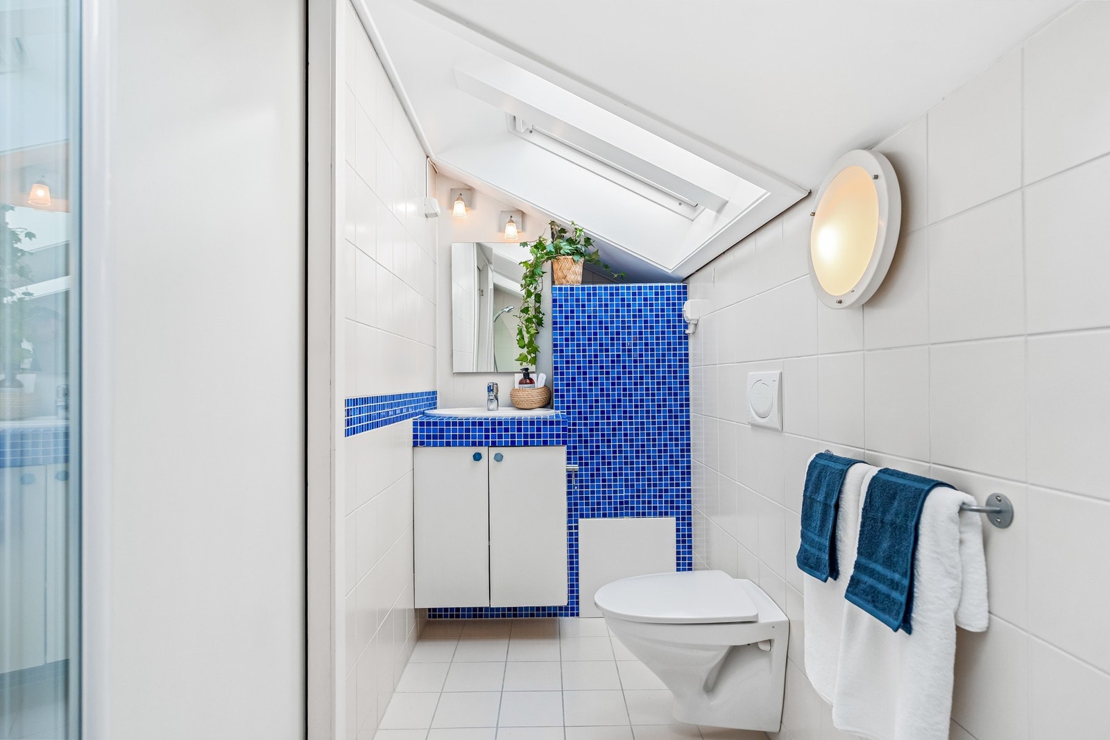 Pent flislagt bad på loftet. Baderomsinnredning med skap og innfliset benkeplate med nedsenket servant og ettgreps blandebatteri. Det er vegghengt toalett og dusj. Galleribilde