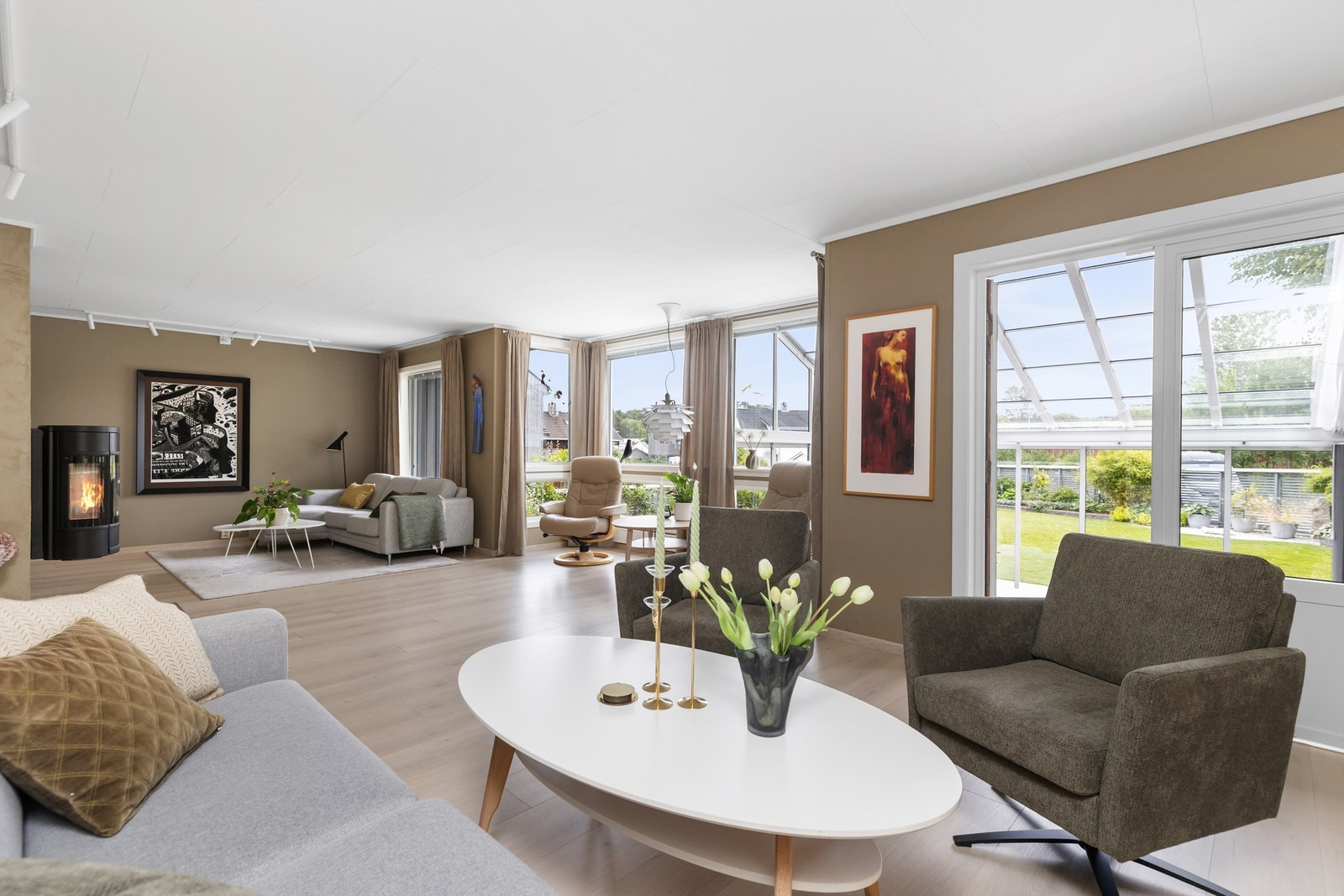 Romslig stue med peisovn og direkte utgang til en innglasset hagestue og hagen.
Foto: Marianne Lyse Galleribilde