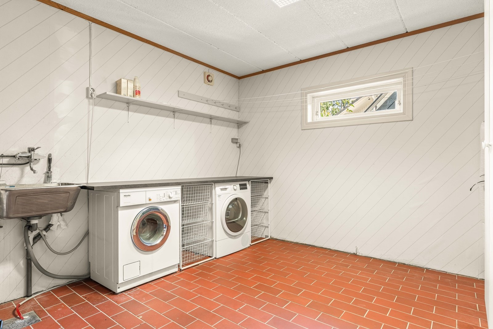 Praktisk vaskerom med flislagt gulv, skyllekum og opplegg for vaskemaskin. Galleribilde