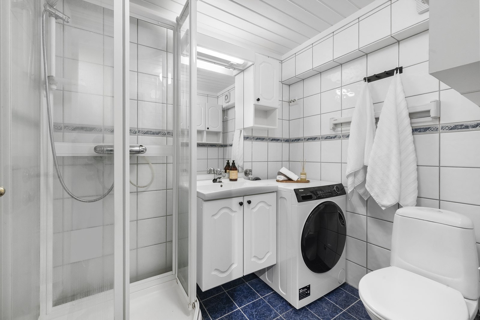 Flislagt bad utstyrt med servant over underskap, speil , dusjkabinett, opplegg til vaskemaskin og wc Galleribilde