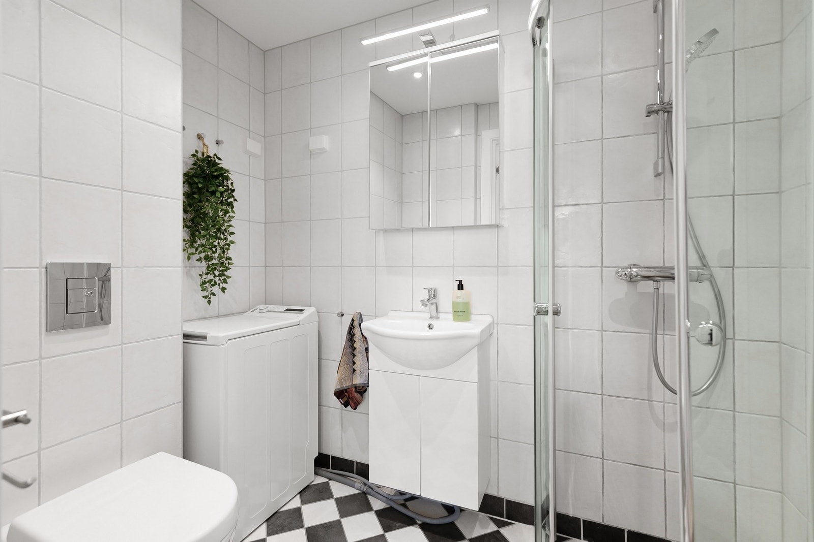Badet er flislagt og innredet med dusjhjørne med buede glassfronter, vegghengt toalett, servantinnredning, speilskap og opplegg for vaskemaskin. Galleribilde