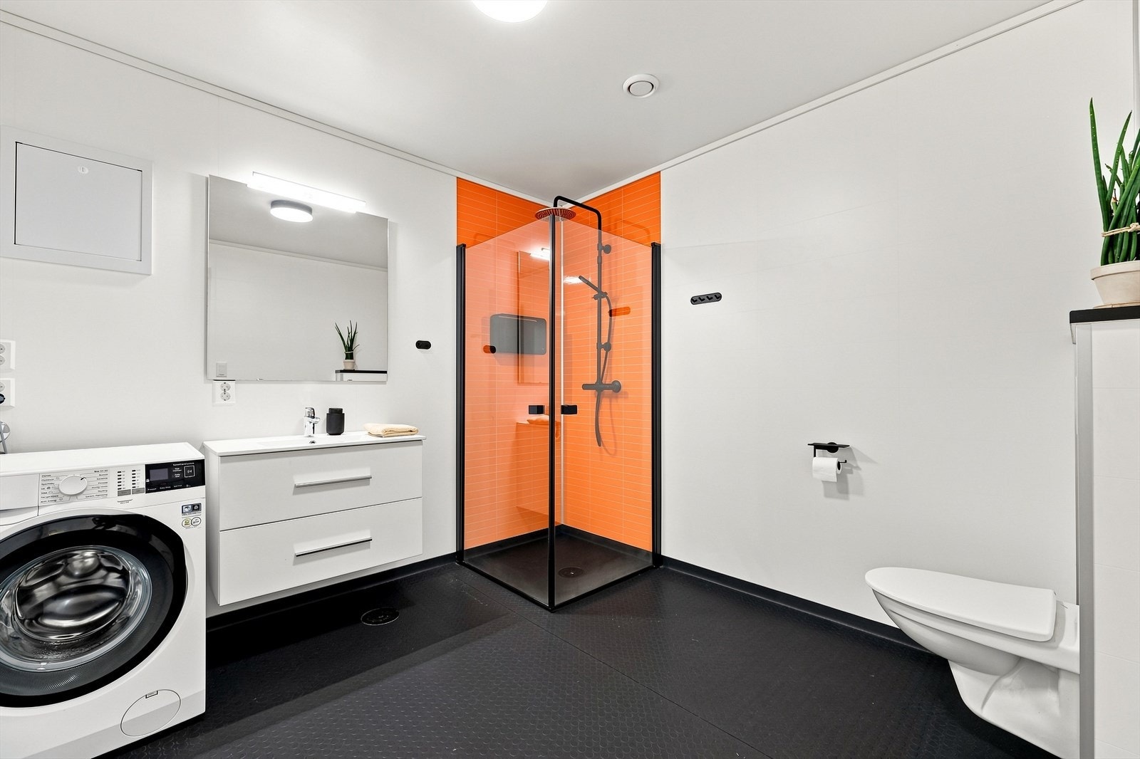 Badet inneholder servantmøbel med slette fronter, speil, vegglampe, opplegg for vaskemaskin/tørketrommel, fordelerskap til rør-i-rør og vegghengt toalett. Her er elektriske varmekabler i gulv og avtrekksventil i himling. Galleribilde