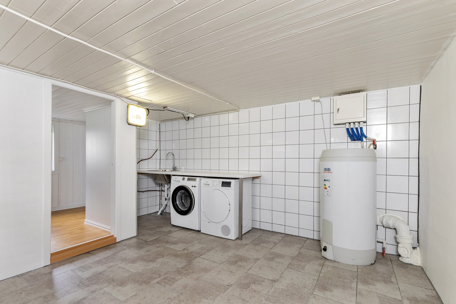 Praktisk vaskerom med fliser på gulv, utslagsvask og opplegg for vaskemaskin. Varmtvannsberederen på 200 liter er fra 2020. Galleribilde