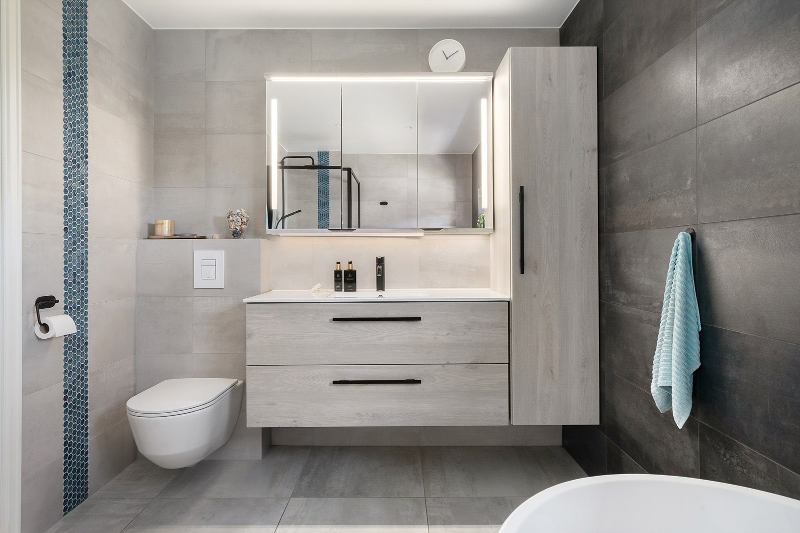 Badet fra 2019 har flislagt gulv med varmekabler, downlights i taket og en moderne innredning med overskap med speil og belysning. Galleribilde