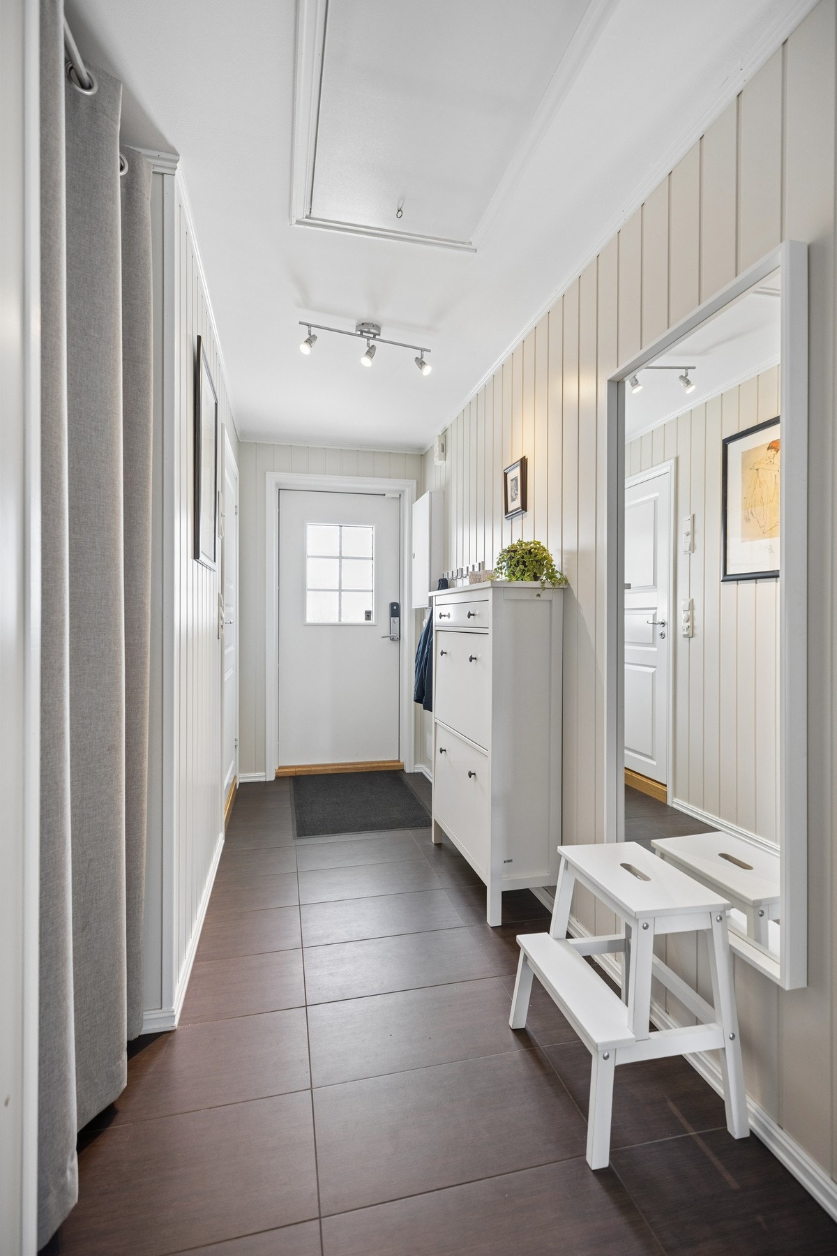 Velkommen inn! Entréen har praktiske flislagte gulv, lyse smartpanelvegger og et tidløst uttrykk. Her er det gode muligheter for oppbevaring av yttertøy og sko. Galleribilde