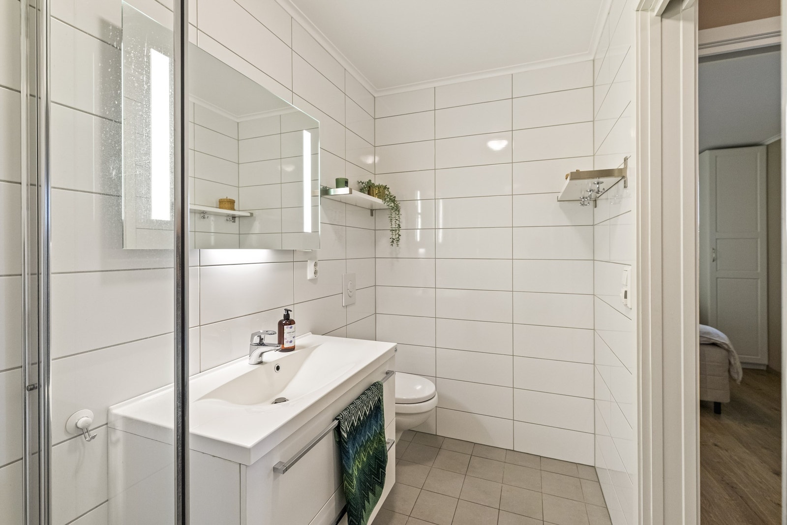 Badet er utstyrt med en elegant dusjsone i hjørnet med glassfelt og glassdør, samt vegghengt toalett som gir et moderne og ryddig uttrykk. Galleribilde