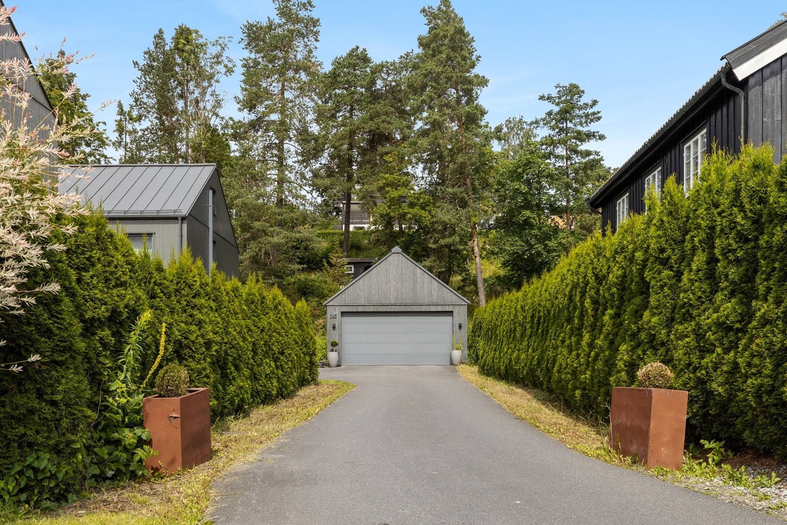 Den private innkjørselen, omkranset av trær på begge sider, leder opp til en romslig asfaltert gårdsplass og gir boligen en representativ ankomst Galleribilde