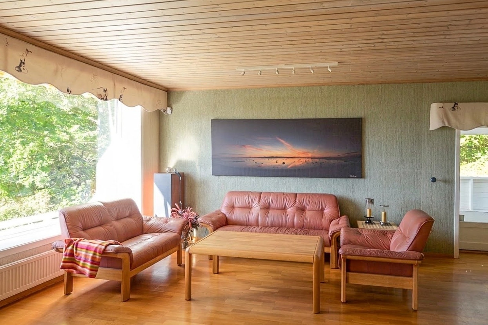 Romslig og lys stue med parkettgulv, strietapet på vegger og panelbord i himling. Fjordutsikt fra vindu. Galleribilde