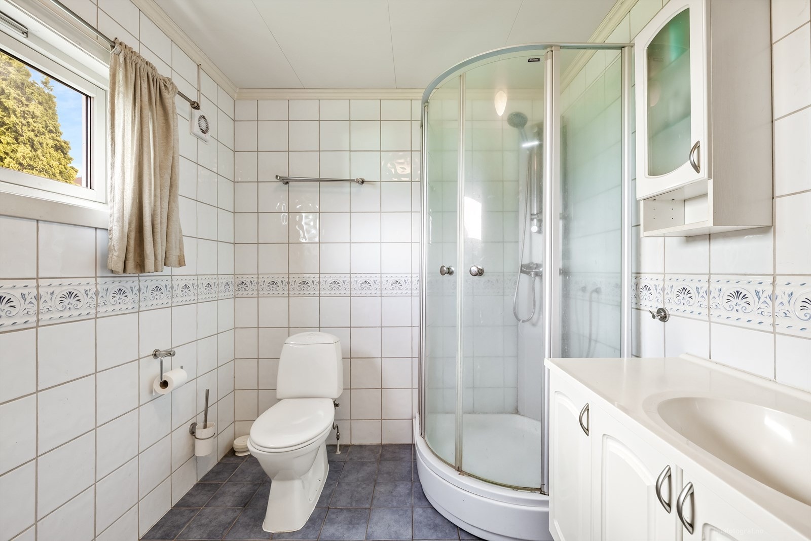 Badet er innredet med toalett, dusjkabinett og servant med underskap. Galleribilde