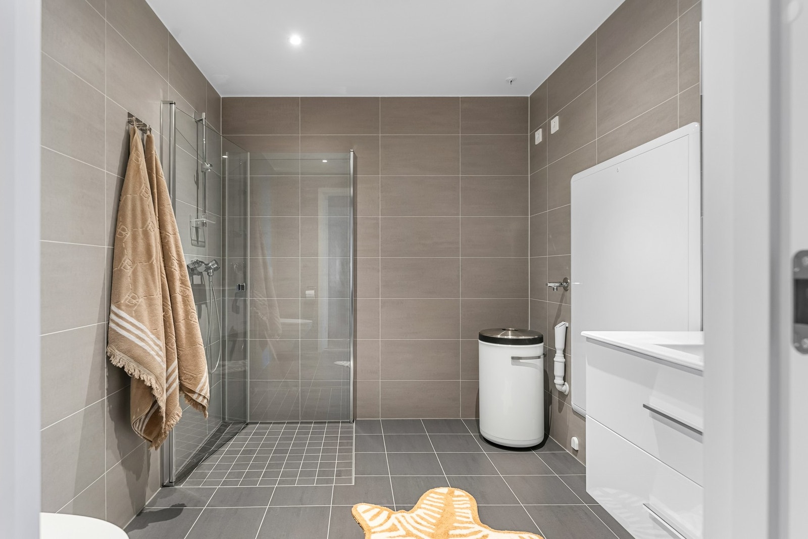 Badet er av god størrelse med vegghengt toalett, opplegg for vaskemaskin og tørketrommel og dusjhjørne med stilrene glassdører. Galleribilde