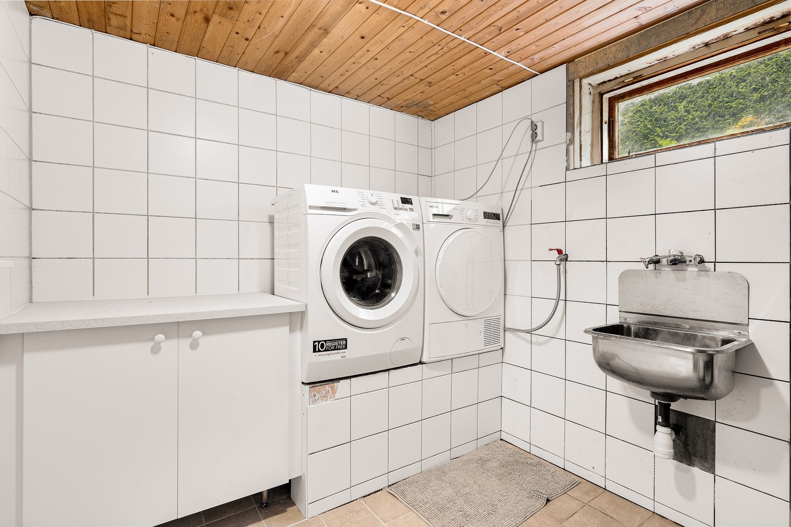 Praktisk vaskerom i kjelleren med flislagt gulv med varmekabler, opplegg for vaskemaskin og tørketrommel. Galleribilde