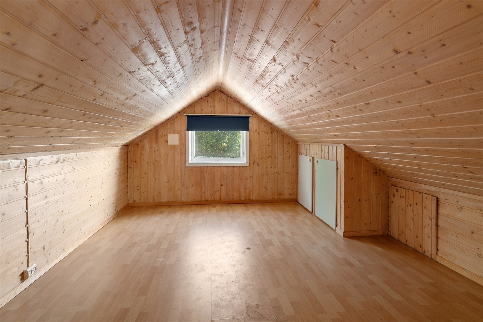 Soverom med panelkledd skråtak, laminatgulv og vindu. Innebygde skap gir praktiske oppbevaringsmuligheter. Galleribilde
