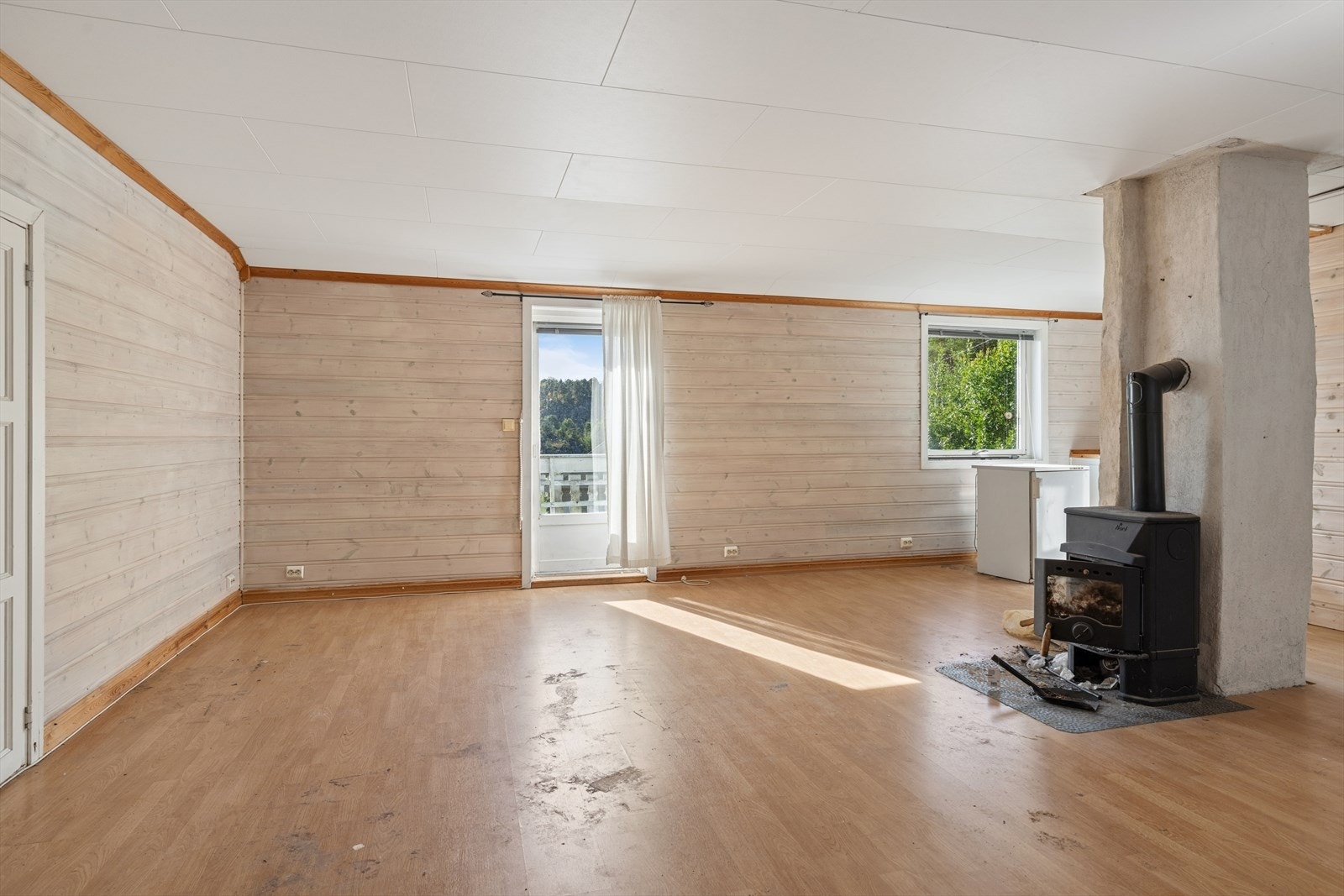 Stue med hvitbeiset, liggende panel på veggene, laminatgulv og vedfyrt peis. Fra stuen er det direkte adkomst til balkongen. Galleribilde