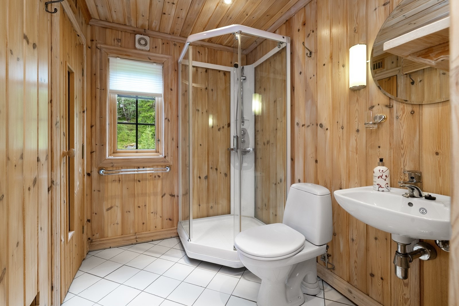 Badet har flislagt gulv med gulvvarme, dusjkabinett og vegghengt servant. Galleribilde