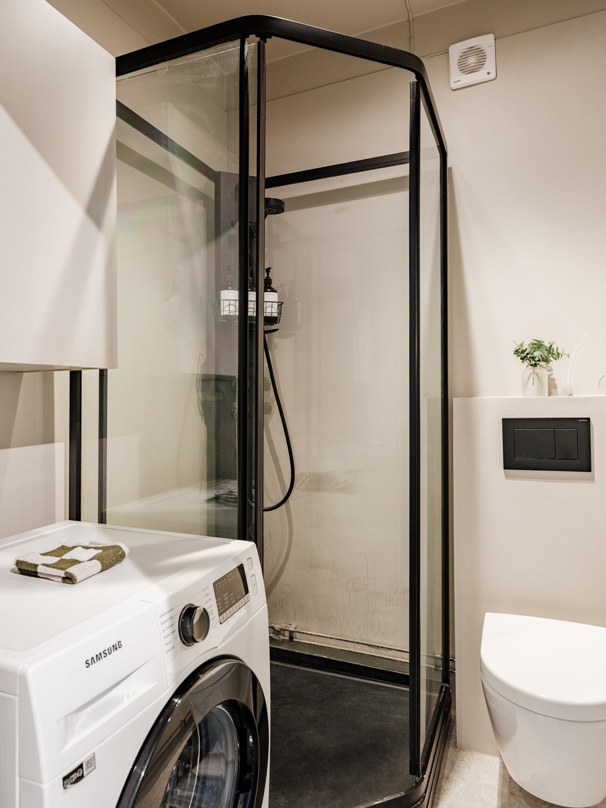 Badet er effektivt innredet med dusjkabinett, vegghengt toalett, servant, vegghengt skap og opplegg for vaskemaskin Galleribilde