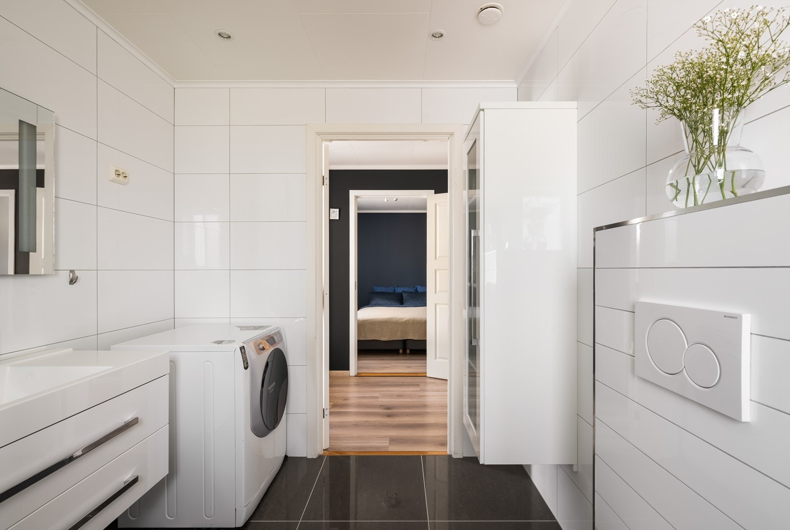 Det inneholder servant i møblement, vegghengt skap, speil m/belysning, dusjhjørne og vegghengt toalett. Badet har opplegg for vaskemaskin og tørketrommel. Galleribilde