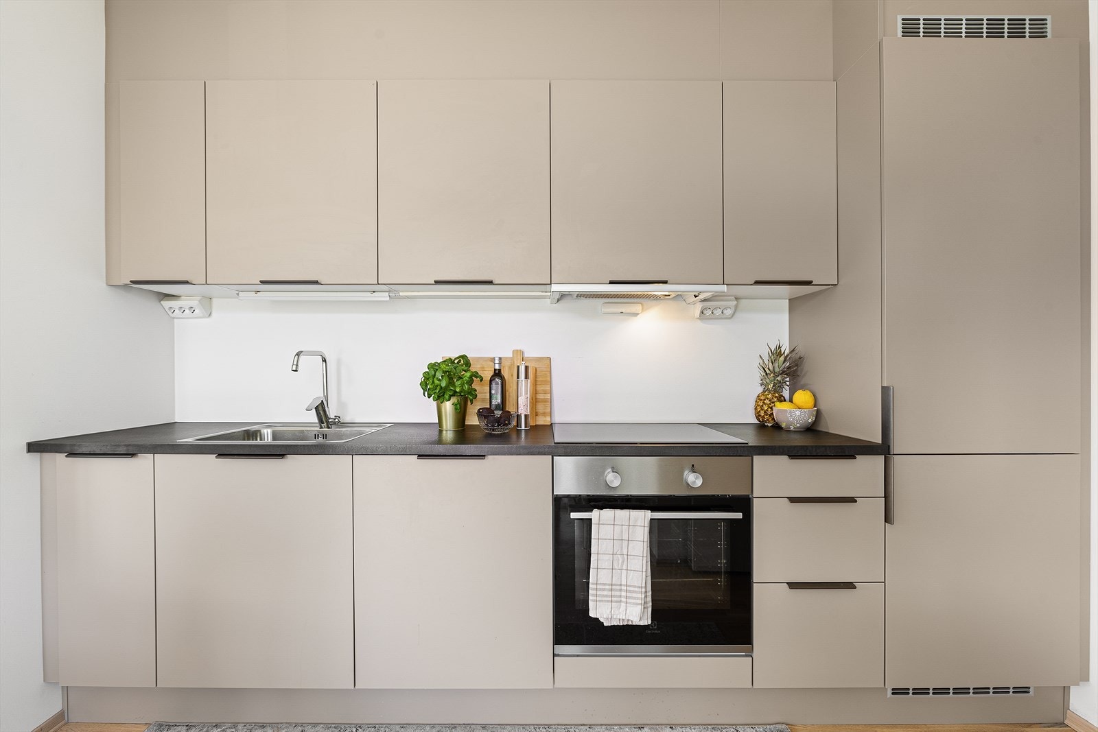 Kjøkkeninnredningen har fått et løft opp fra det klassiske hvite kjøkkenet, og har blitt innredet med slitesterke og slette fronter i en moderne beige farge fra kvalitetsleverandøren HTH. Galleribilde
