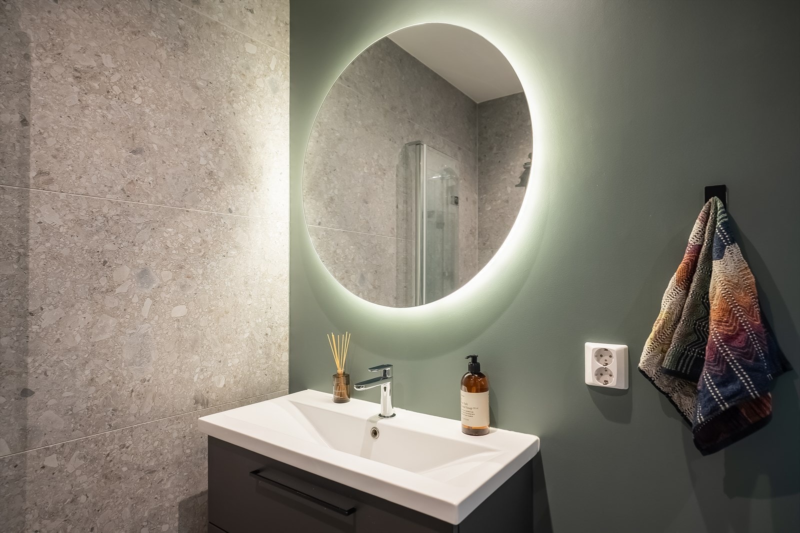 Badet innehar vegghengt toalett, dusjhjørne, baderomsinnredning med helvask, speil med integrert belysning og opplegg for vaskemaskin. Galleribilde