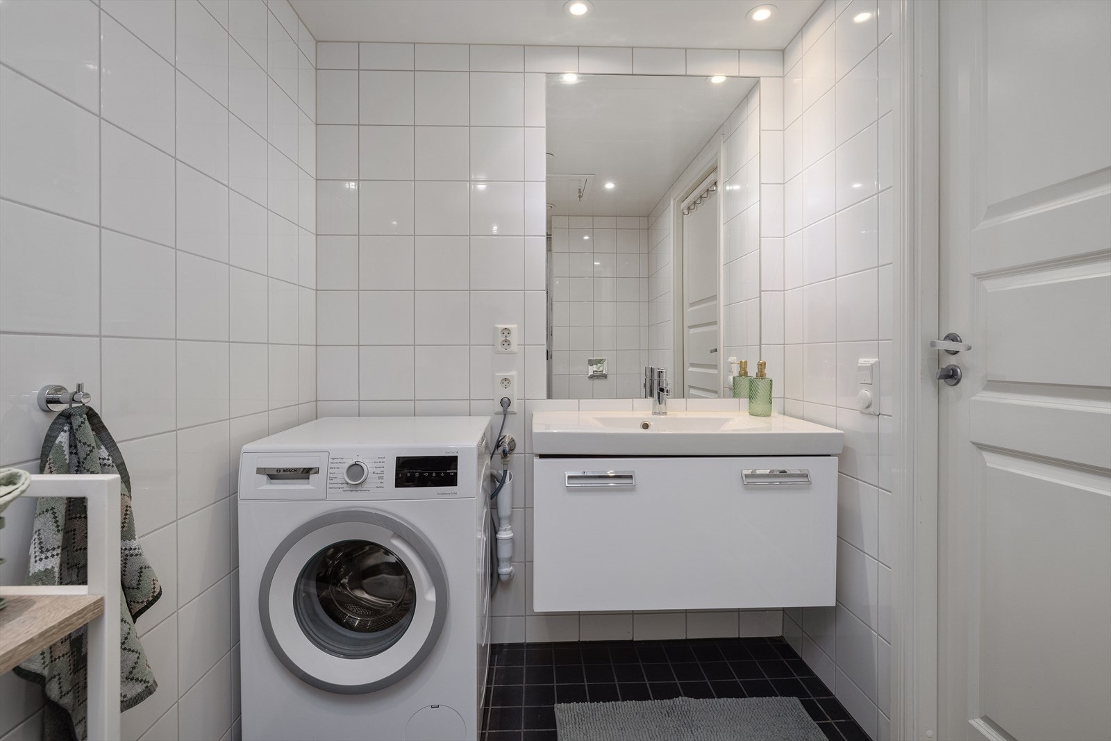Badet er flislagt på gulv og vegger, med himlingsplater i taket. Innredningen består av nedfelt servant, veggmontert toalett og dusjvegger/hjørne. Galleribilde