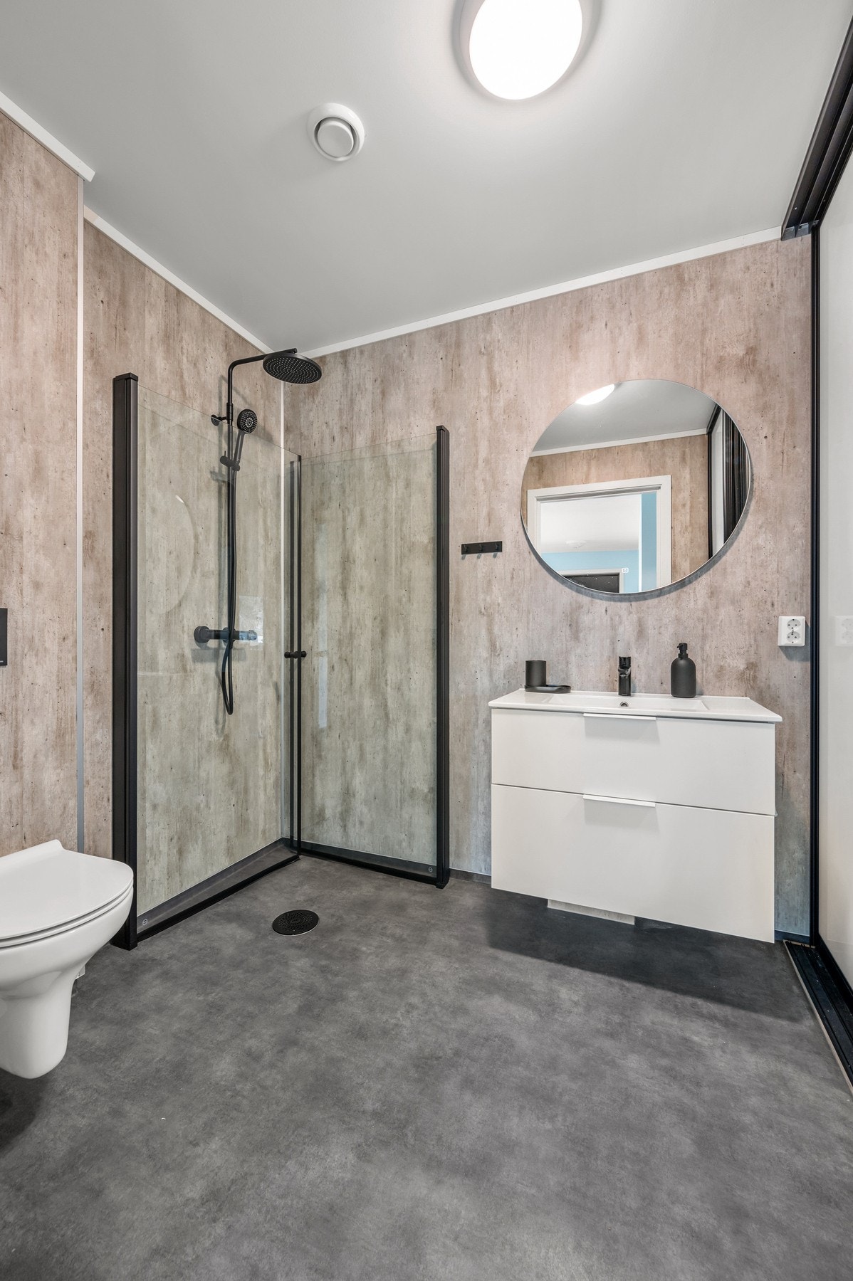 Moderne og delikat bad med gjennomførte materialvalg og et stilrent uttrykk. Badet er innredet med elegant servantmøbel, og rundt speil med belysning. Dusjsonen er romslig og avskjermet med glassvegger, mens vegghengt toalett bidrar til et moderne og rydd Galleribilde