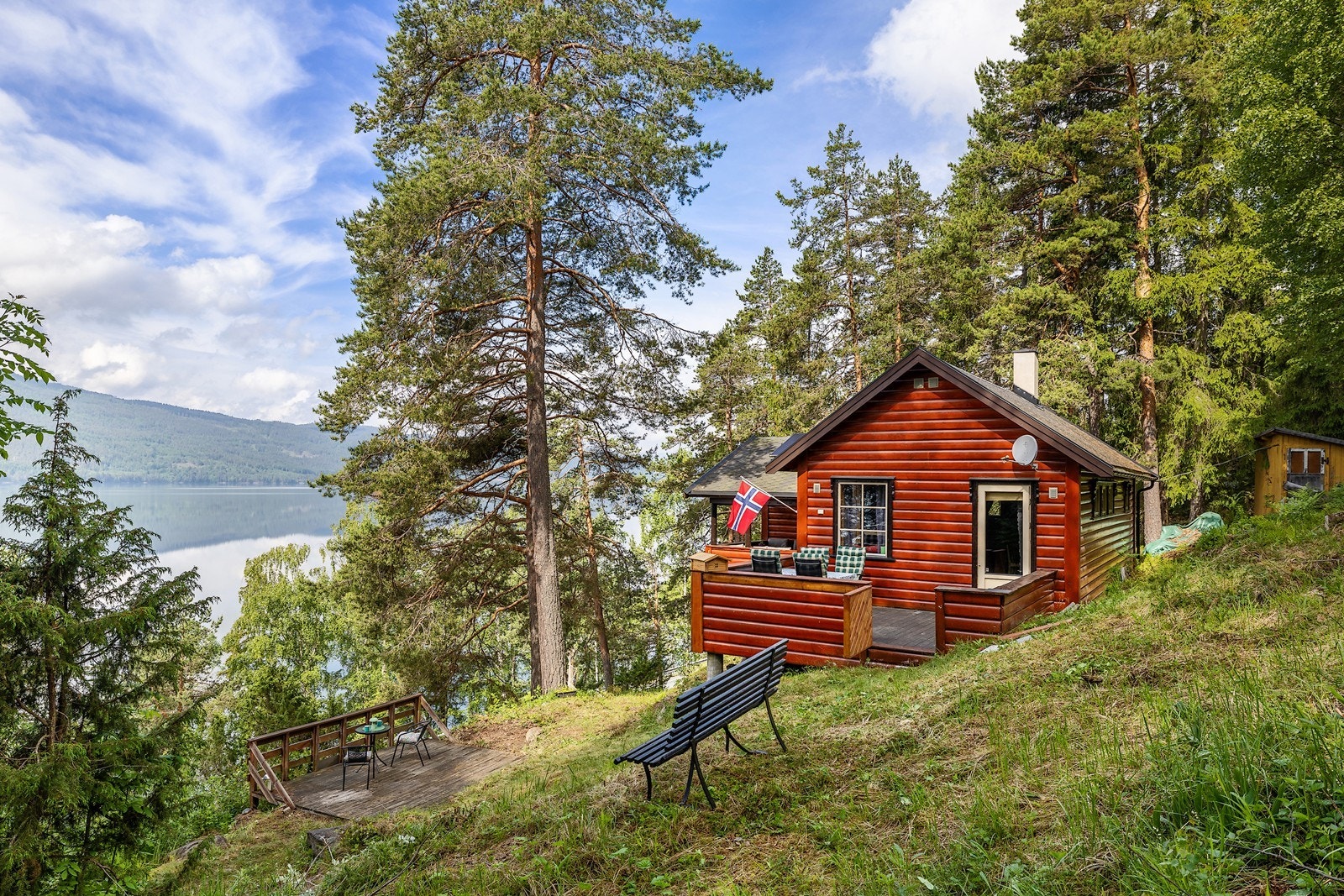 Hytta ligger i skrånende terreng med utsikt over vannet. Galleribilde