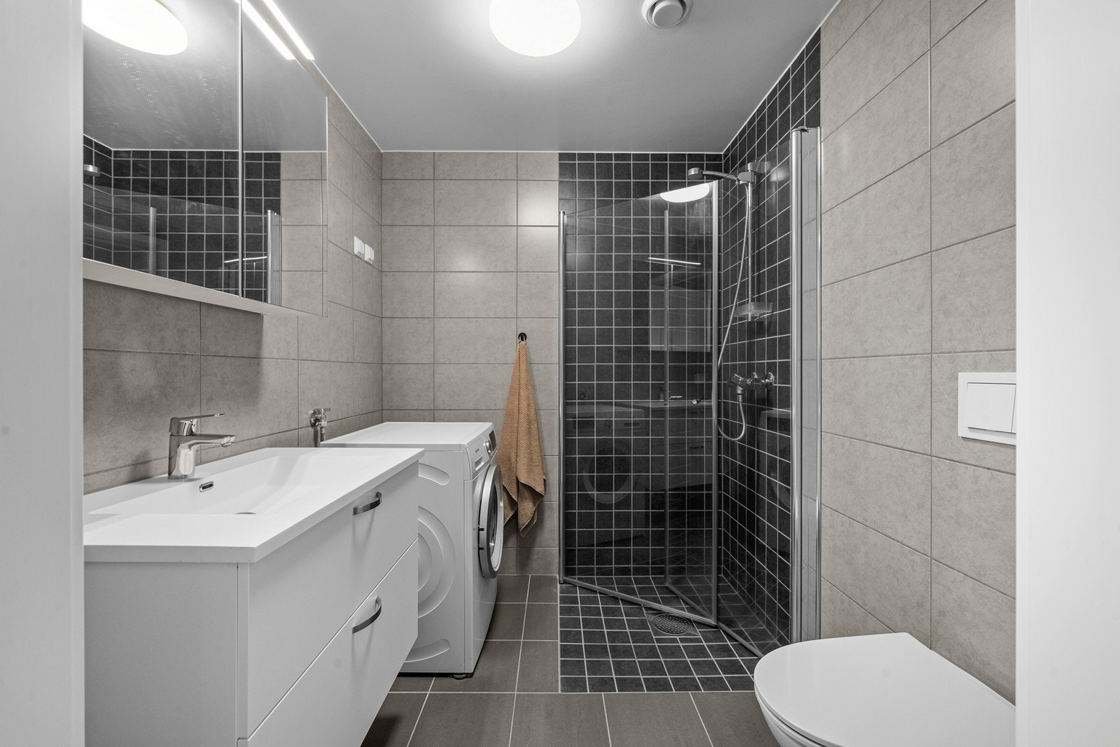 Badet fremstår som moderne med flislagte overflater i stilrene fargetoner. Galleribilde