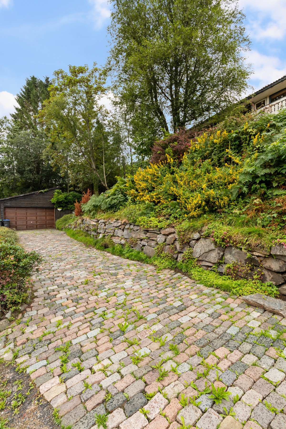 Eiendommen ligger i skrånende terreng og tomten er opparbeidet med belegningsstein i innkjørsel og biloppstillingsplass. Galleribilde