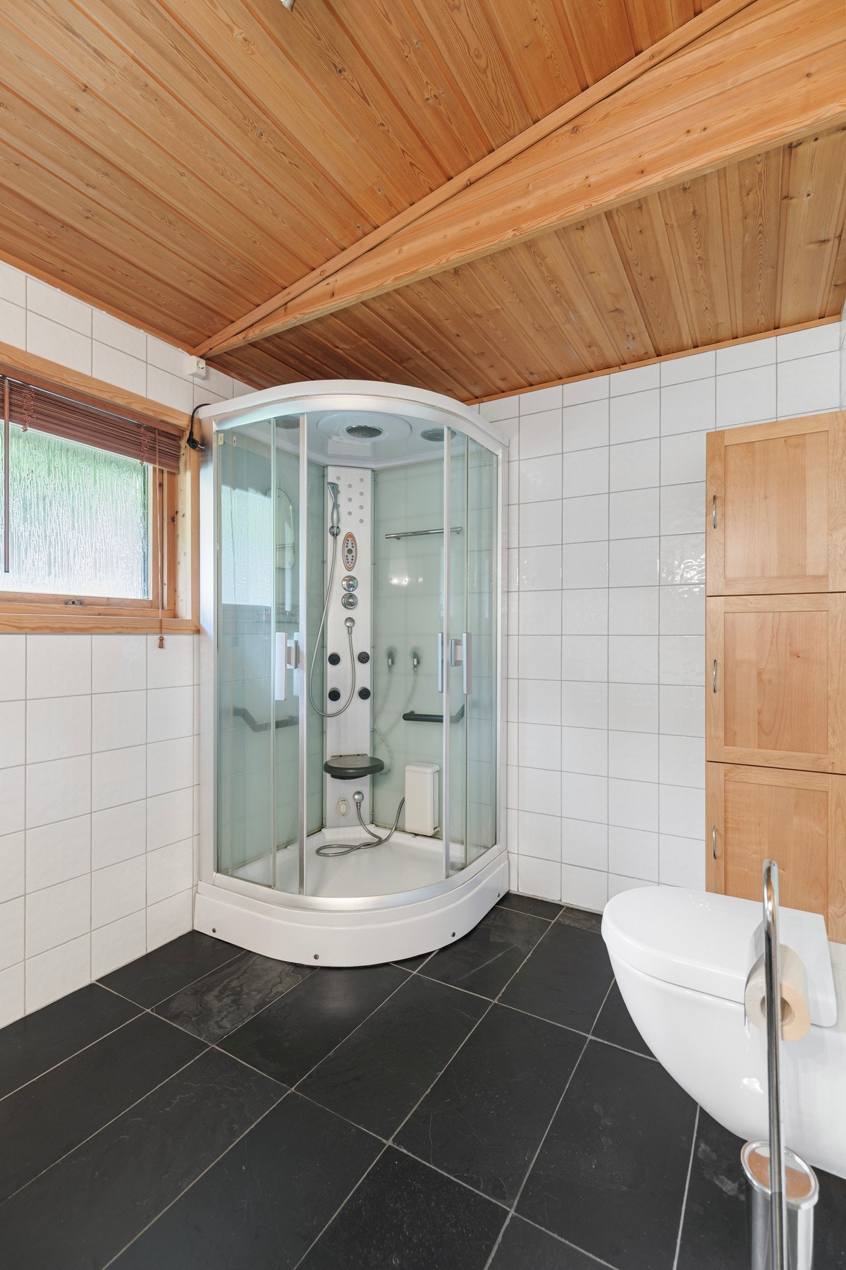 Badet utstyrt med varmekabler i gulv, dusjkabinett med massasjedyser, veggmontert toalett, hel servantplate med to vasker og ventilasjon i himling. Galleribilde