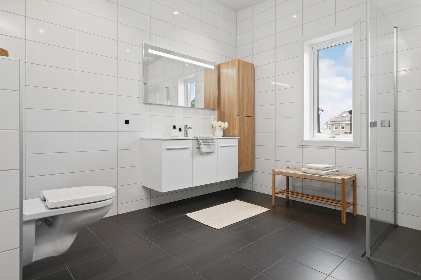 Badet er delikat innredet med hvite veggfliser og mørke gulvfliser for en fin kontrast. Galleribilde