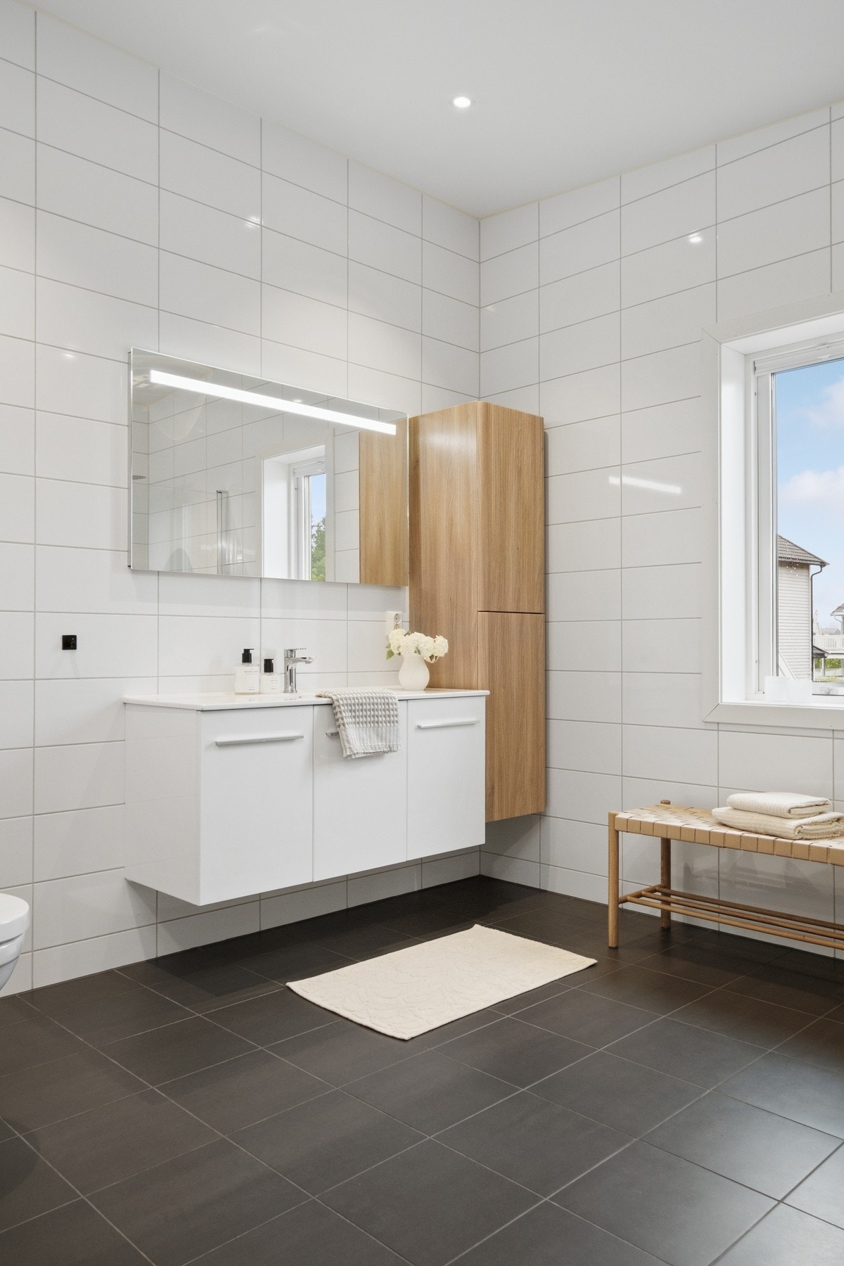 Varme er lagt i gulvet, og begge badene har downlights, vegghengt toalett, et hvitt servantskap og et speil med integrert belysning. Galleribilde