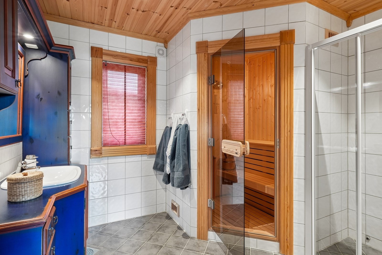 Badet i første etasje har baderomsinnredning i aldringsmalt heltre med over- og underskap, speil med tilhørende belysning, toalett og dusj med glassdør/-vegg. Fra badet er det direkte inngang til badstuen. Galleribilde
