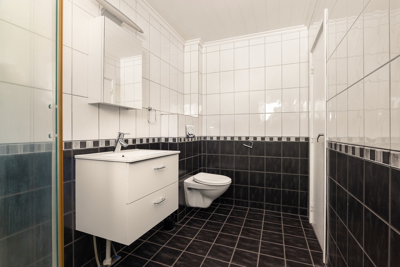 Badet er pent utstyrt med mørke fliser på gulv, lyse fliser på vegg, gulvvarme og speilskap med overbelysning. Galleribilde