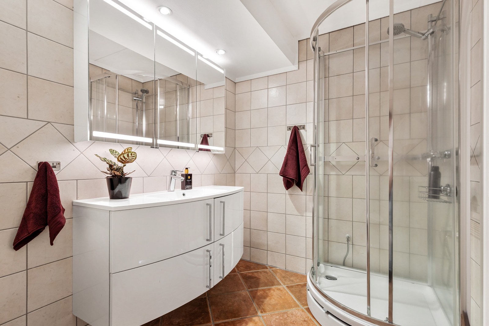 Badet er innredet med dusjkabinett, gulvstående toalett og servant med underskap- og overskap med LED lys Galleribilde