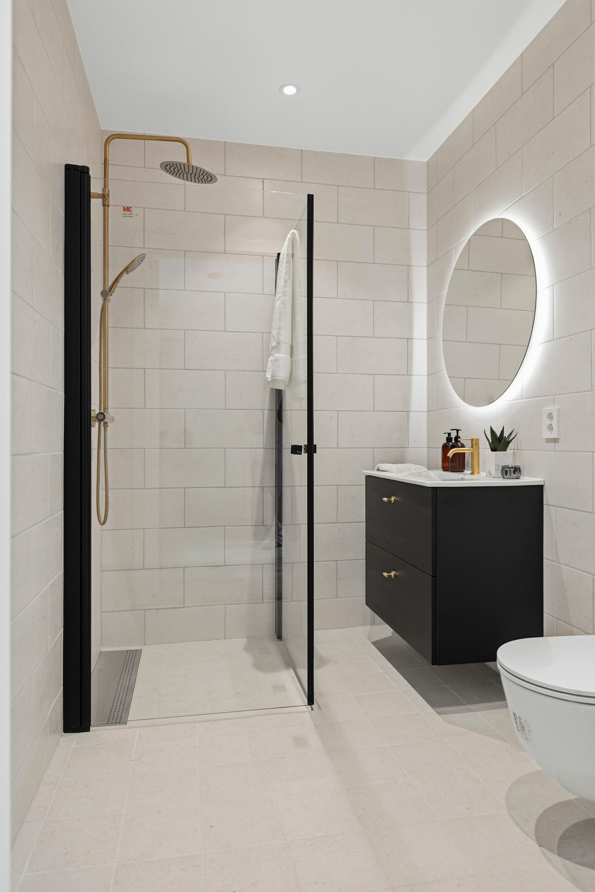 Badet fremstår moderne og gjennomført, med lyse fliser som kombineres elegant med sorte og messingfargede detaljer. Galleribilde