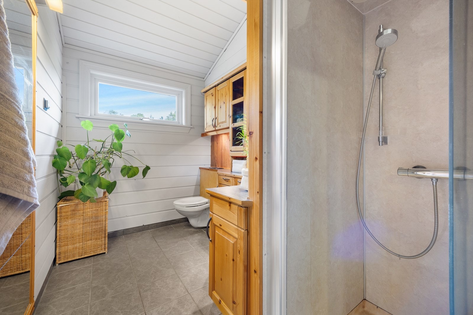 Badet har fliser på gulvet og trepaneler på veggene, samt en dusjsone med belegg og baderomsplater. Galleribilde