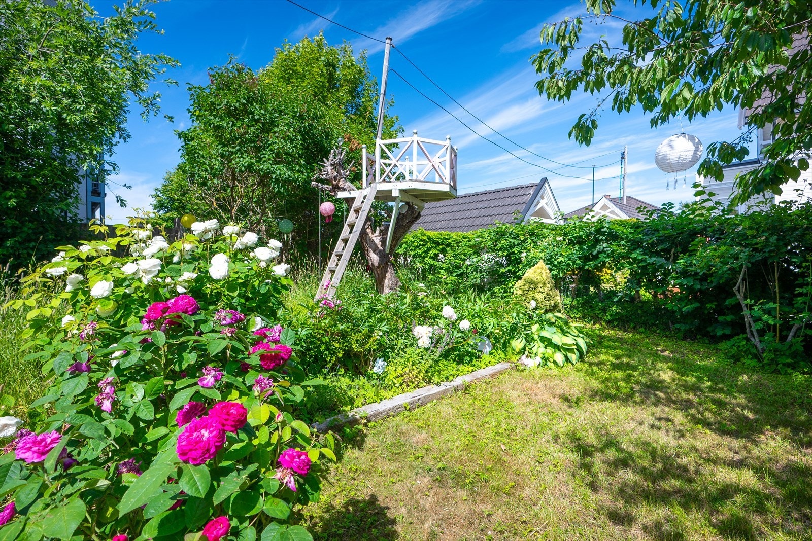 Den frodige hagen er opparbeidet med beplantning, blomstrende busker og trær som skaper en lun og idyllisk ramme rundt boligen. Galleribilde