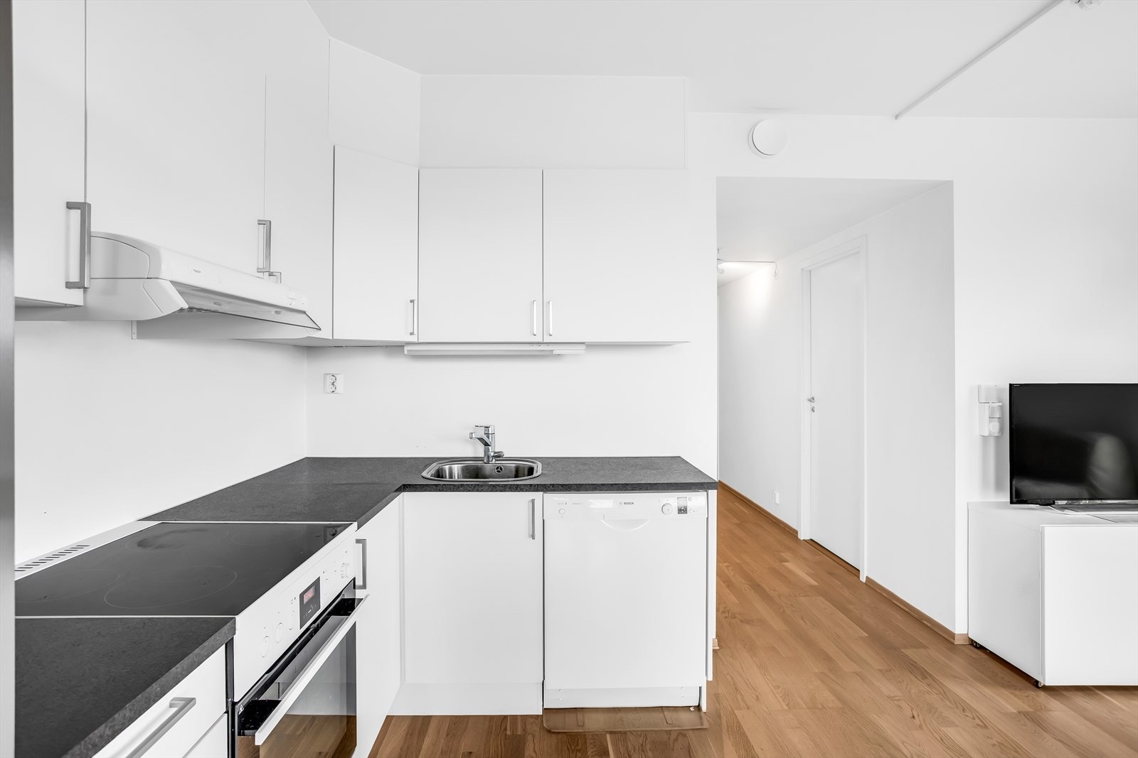 Kjøkkeninnredningen har hvite, glatte fronter og laminatbenkeplate. Det er opplegg for oppvaskmaskin. Galleribilde