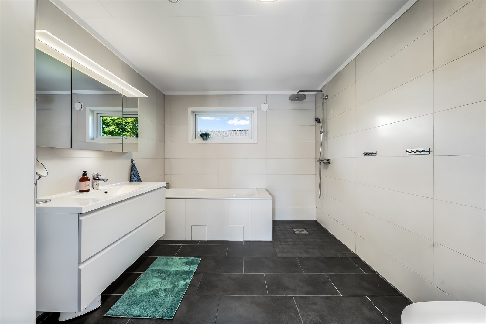 Badet har en moderne og tiltalende utforming med store fliser, vegghengt baderomsinnredning og god plass til både badekar og dusjsone. Rommet fremstår lyst, romslig og funksjonelt. Galleribilde