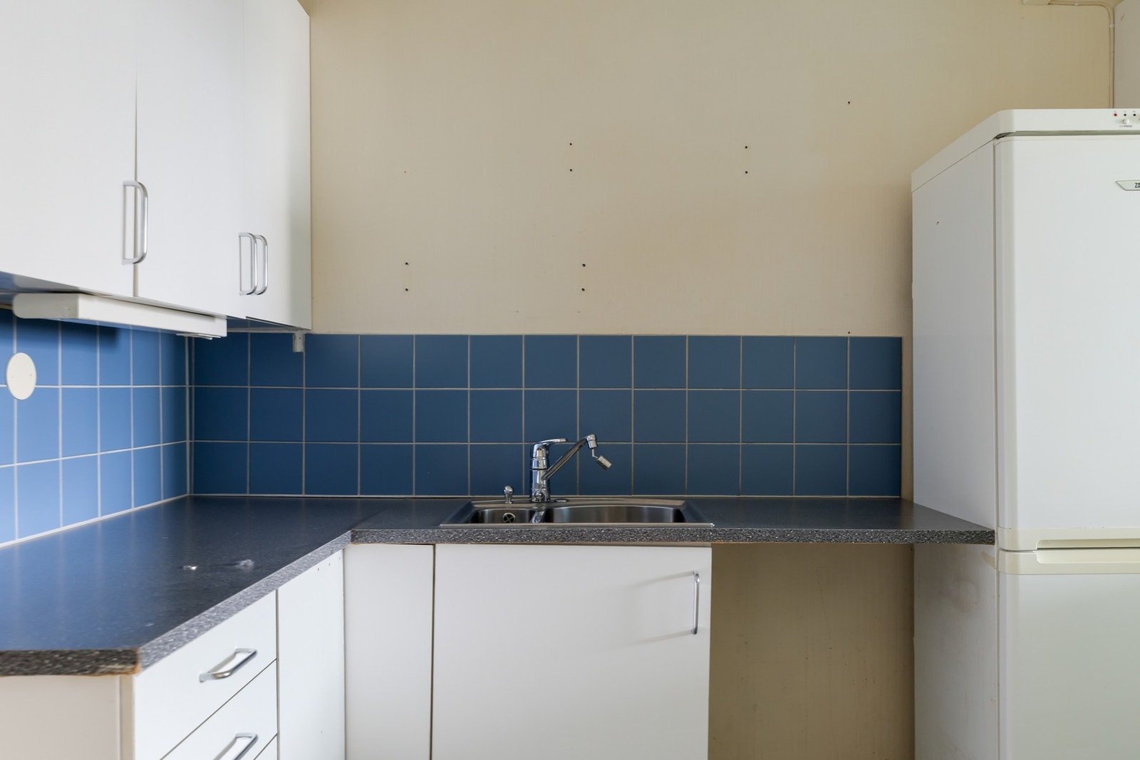 Kjøkken med profilerte fronter, fliser over benkeskap og laminat benkeplate med nedfelt kum i rustfritt stål. Galleribilde