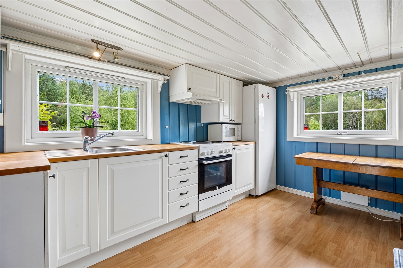 Hyggelig, landsens kjøkken med hvitmalt innredning og en solid benkeplate i heltre. Galleribilde