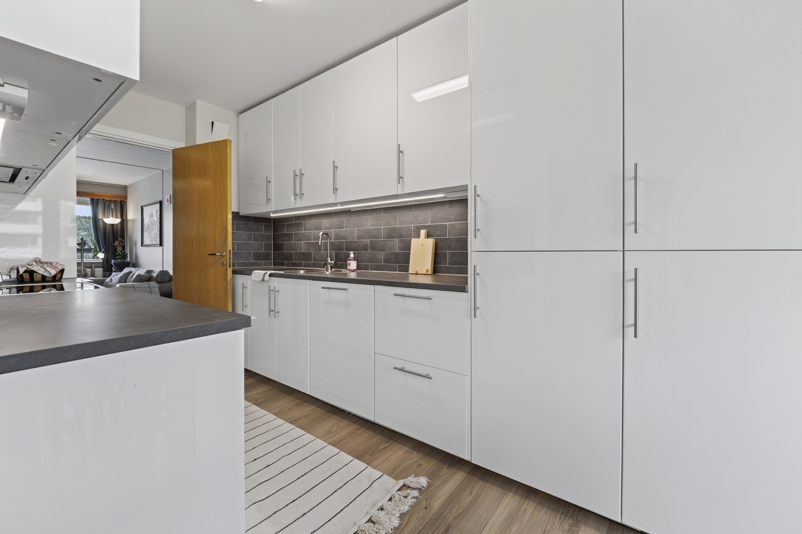 Kjøkken med moderne, hvite fronter og mørk laminat benkeplate. Galleribilde