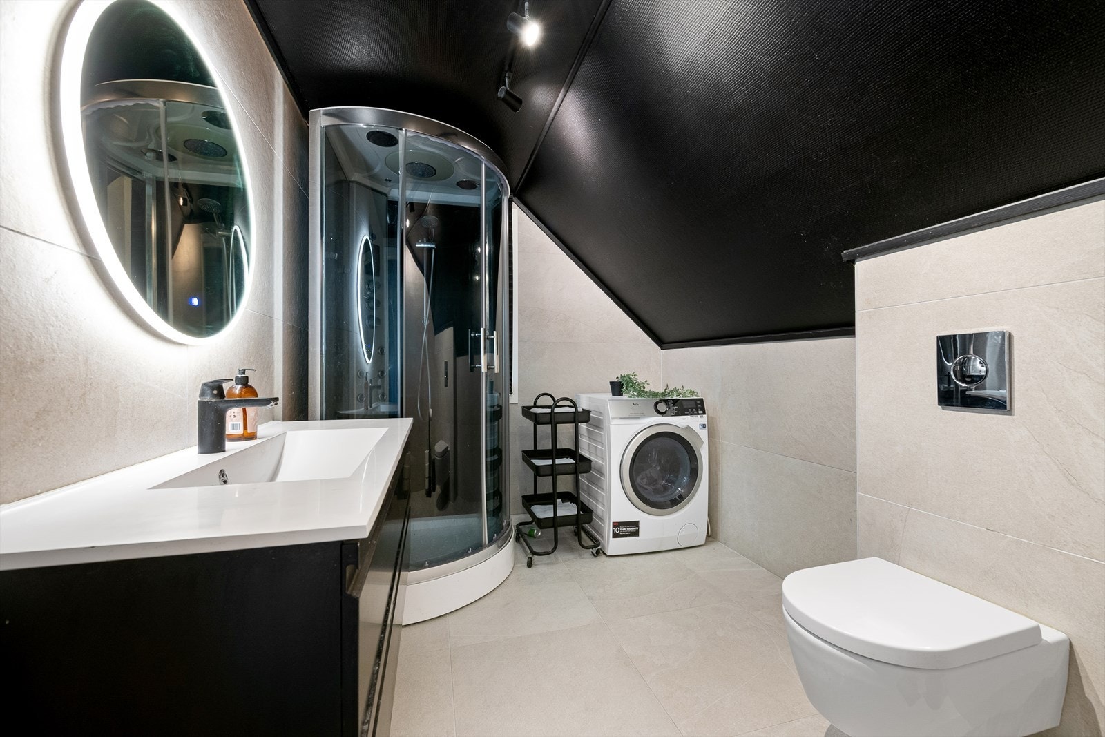 Badet i loftsetasjen har flislagte overflater, dusjkabinett, og opplegg for vaskemaskin. Galleribilde