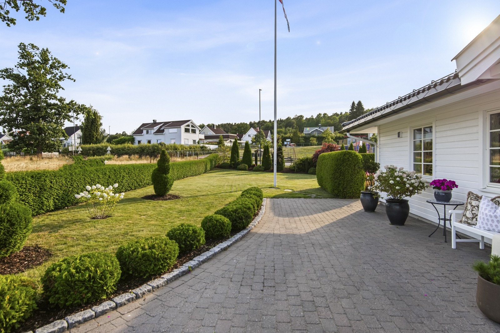 Den steinbelagte gårdsplassen strekker seg rundt hushjørnene og videre mot garasjen, hvor det er etablert en uteplass med deilig morgensol. Galleribilde