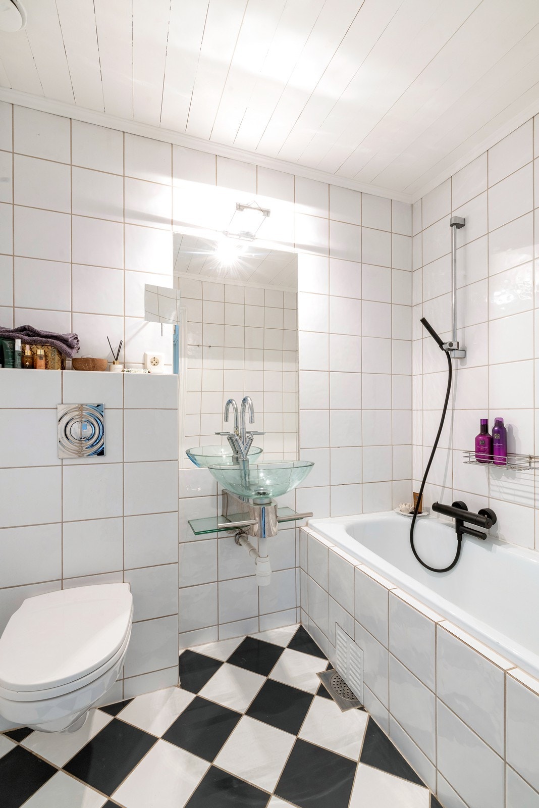 Badet har et stilig sjakkmønster på gulv, vegghengt klosett og servant i glass. Galleribilde