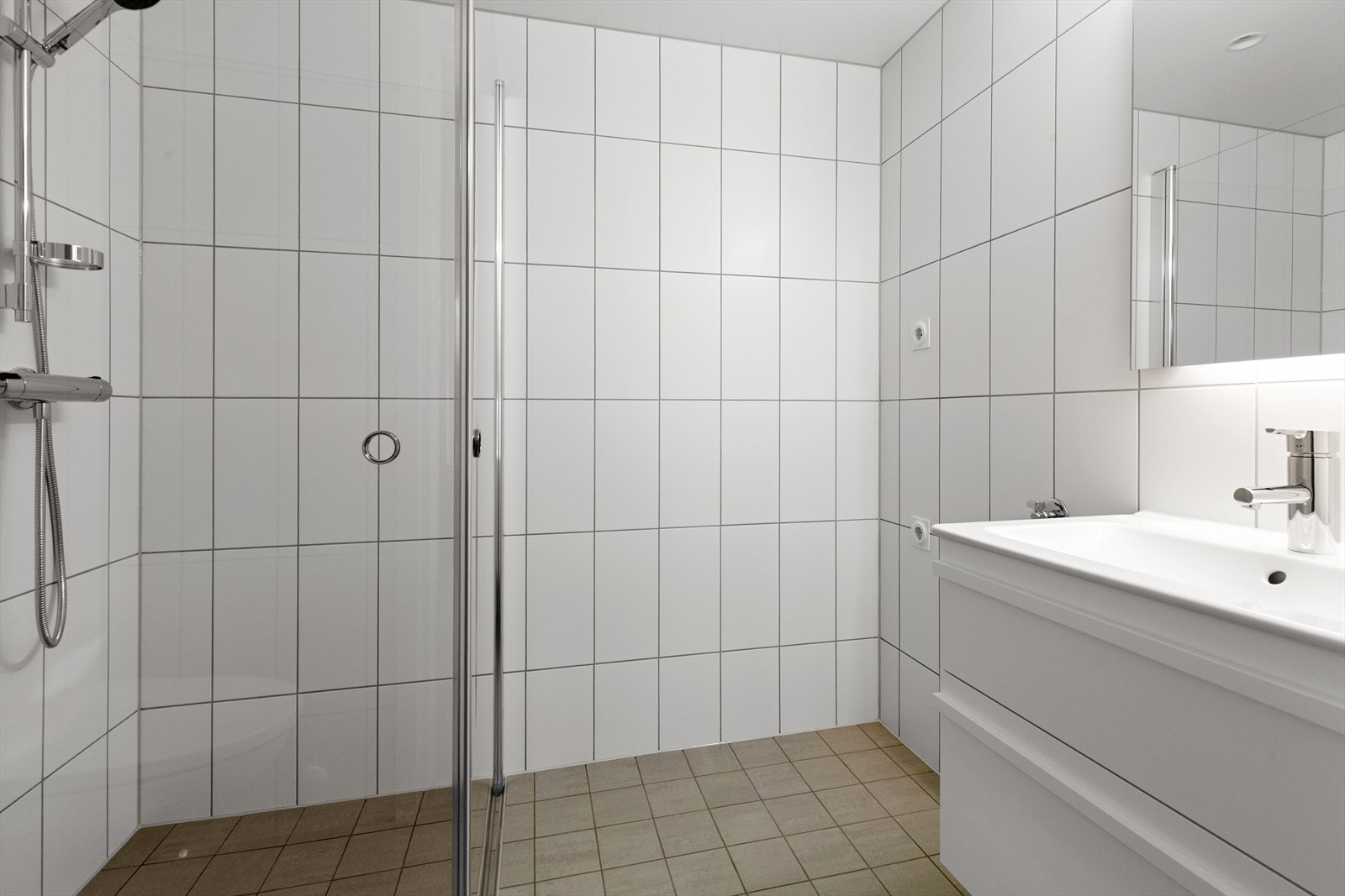 Badet er innredet med skuffeseksjon med nedfelt servant og stikkontakt i innredningen, veggmontert toalett fra TECE, svingbare dusjvegger i glass samt opplegg for vaskemaskin. Galleribilde