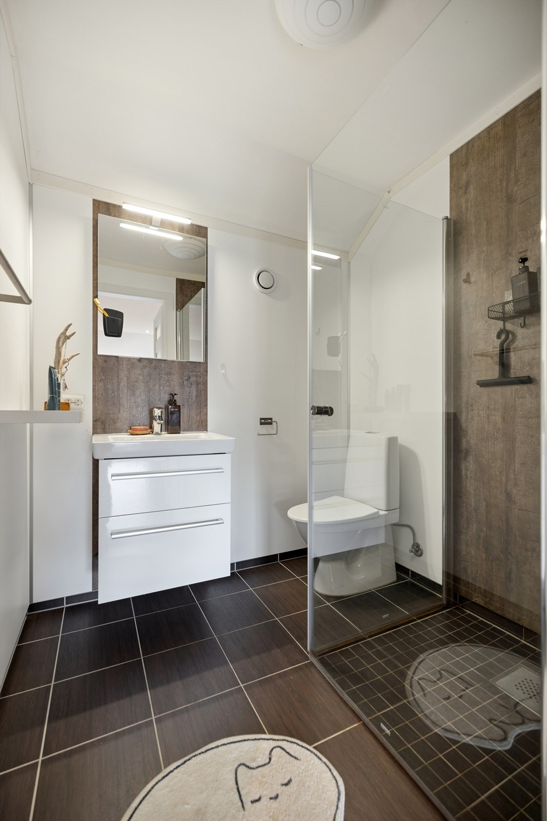 Badet i loftsetasjen har våtromsplater på vegg, malte plater i himling og fliser på gulv med gulvvarme. Innredningen består av servant med underskap, speil, dusjdører og gulvmontert toalett. Galleribilde