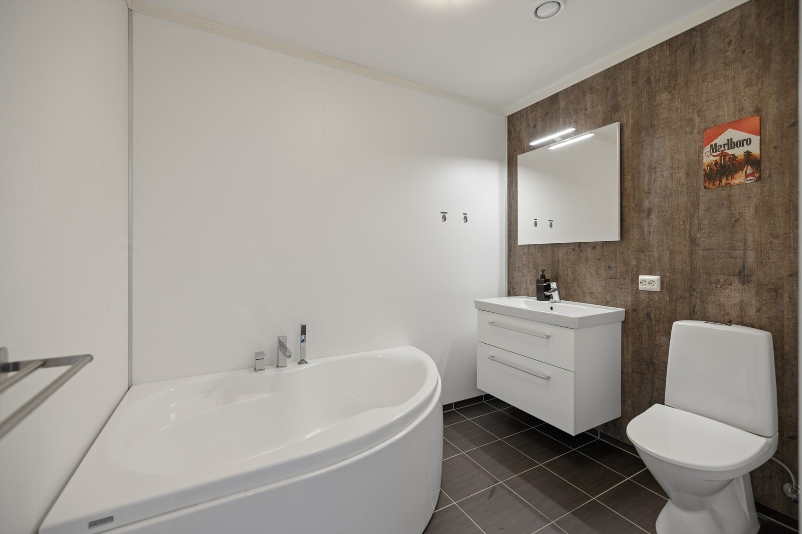 Badet i 1. etasje har våtromsplater på vegg og fliser på gulv med gulvvarme. Innredningen består av dobbelservant med underskap, speil, badekar og gulvmontert toalett. Galleribilde