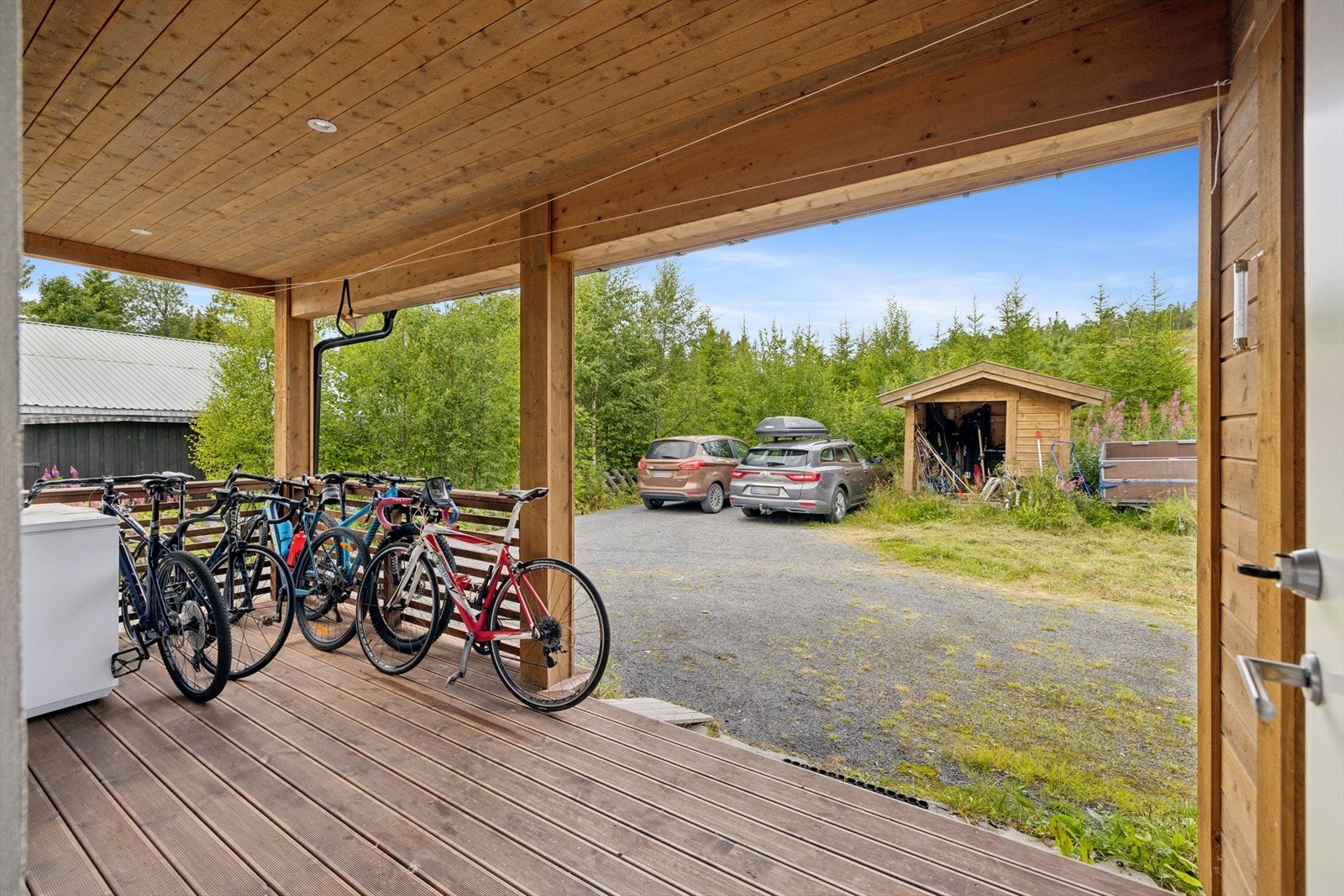 Overbygget inngangsparti og gruset gårdsplass med parkering til flere biler. Galleribilde