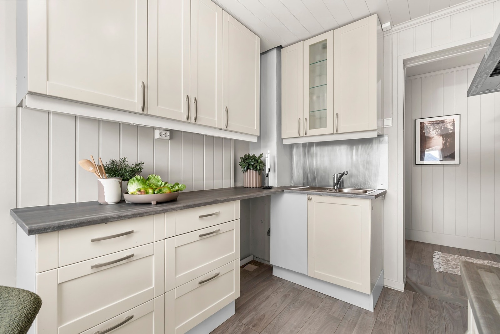 Fliser over deler av benken. Opplegg for oppvaskmaskin. Gulv med laminat, vegger med panelplater og malt tapet. Galleribilde